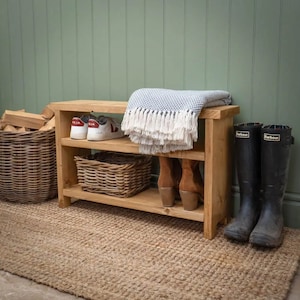 May include: A wooden shoe rack with two shelves and a top shelf for storage. The rack is made of natural wood and has a rustic look. It is filled with shoes, boots, and a blanket.