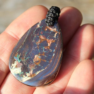 May include: A teardrop-shaped pendant made of black opal with a dark blue, green, and brown iridescent sheen. The pendant is attached to a black cord.