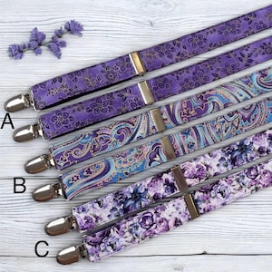 May include: Several purple suspenders with different patterns, including floral and paisley designs. The suspenders have silver clips and gold-coloured adjusters. The patterns include small gold flowers, a blue and purple paisley, and purple floral designs.