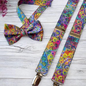May include: A colorful bow tie and suspenders set. The bow tie is tied and the suspenders have metal clips. The fabric features a vibrant pattern of flowers and swirls in shades of blue, yellow, pink, and purple.