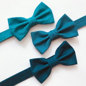 May include: Three teal bow ties with adjustable straps. The bow ties are made of a soft, smooth fabric.