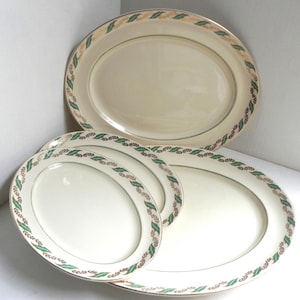 Op de afbeelding: Set van vier ovale serveerschalen met een crèmekleurige achtergrond en een groen en gouden bladontwerp rond de rand.