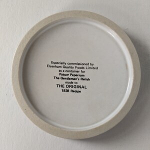 Może przedstawiać: Biała ceramiczna pokrywka do słoika z czarnym tekstem, kt&oacute;ry brzmi: "Especially commissioned by Elsenham Quality Foods Limited as a container for Patum Peperium The Gentleman's Relish made to THE ORIGINAL 1828 Recipe"