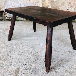 Pode incluir: Uma mesa de centro de madeira castanho escura com um tampo rústico e irregular e quatro pernas robustas. A mesa tem um acabamento natural e desgastado.
