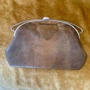 Op de afbeelding: Een gestructureerde clutch met een textuur van hagedissenhuid in bruin- en grijstinten. De tas heeft een zilverkleurig metalen frame met een sluiting aan de bovenkant en een decoratief driehoekig lipje in het midden van het voorpaneel.