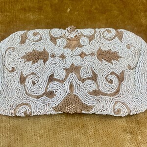 May include: An ivory beaded clutch bag with a decorative floral pattern in shades of brown. The bag has a rectangular shape with a clasp closure. The beads are small and tightly packed, creating a textured surface.