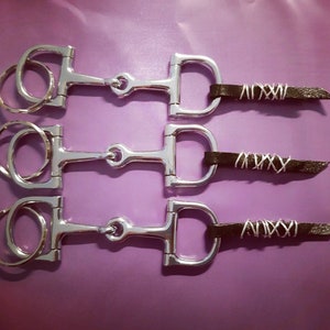 May include: Three silver keychains with black leather straps. Each strap has a silver wire design that reads "XIXXI".