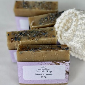 Puede incluir: Barras de jab&oacute;n rectangulares de color tostado cubiertas con brotes de lavanda secos. Cada barra est&aacute; envuelta en una etiqueta de papel morado claro con el texto Simply Sublime Soaps, Lavender Soap, Savon &agrave; la Lavande y 100 g.