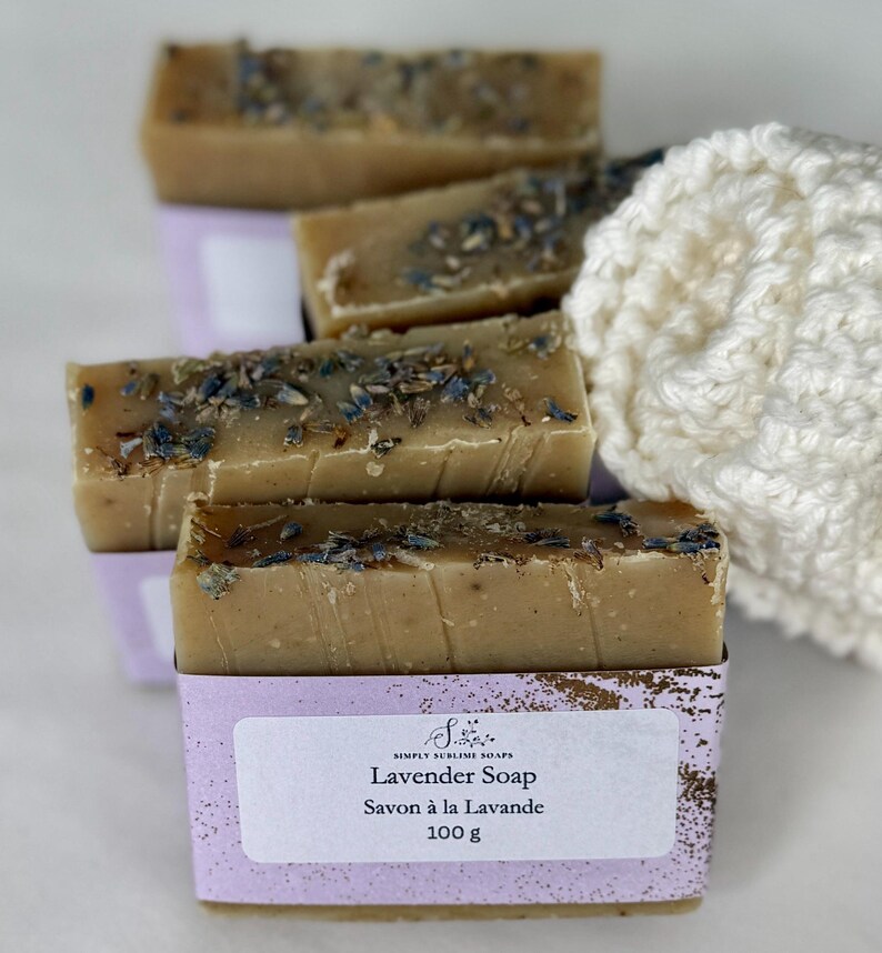 Puede incluir: Barras de jab&oacute;n rectangulares de color tostado cubiertas con brotes de lavanda secos. Cada barra est&aacute; envuelta en una etiqueta de papel morado claro con el texto Simply Sublime Soaps, Lavender Soap, Savon &agrave; la Lavande y 100 g.
