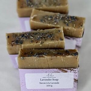 Puede incluir: Cuatro barras de jab&oacute;n rectangulares de color beige cubiertas con brotes de lavanda secos. Cada barra est&aacute; envuelta en una banda de papel de color violeta claro con el texto Simply Sublime Soaps, Lavender Soap, Savon &agrave; la Lavande, 100 g.
