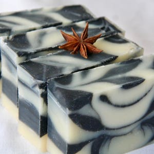 May include: Four bars of handmade soap with a black and white swirl pattern. The soap is arranged in a stack with a star anise on top.