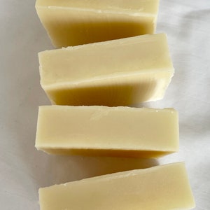 May include: Four bars of plain white soap stacked on top of each other on a white surface.