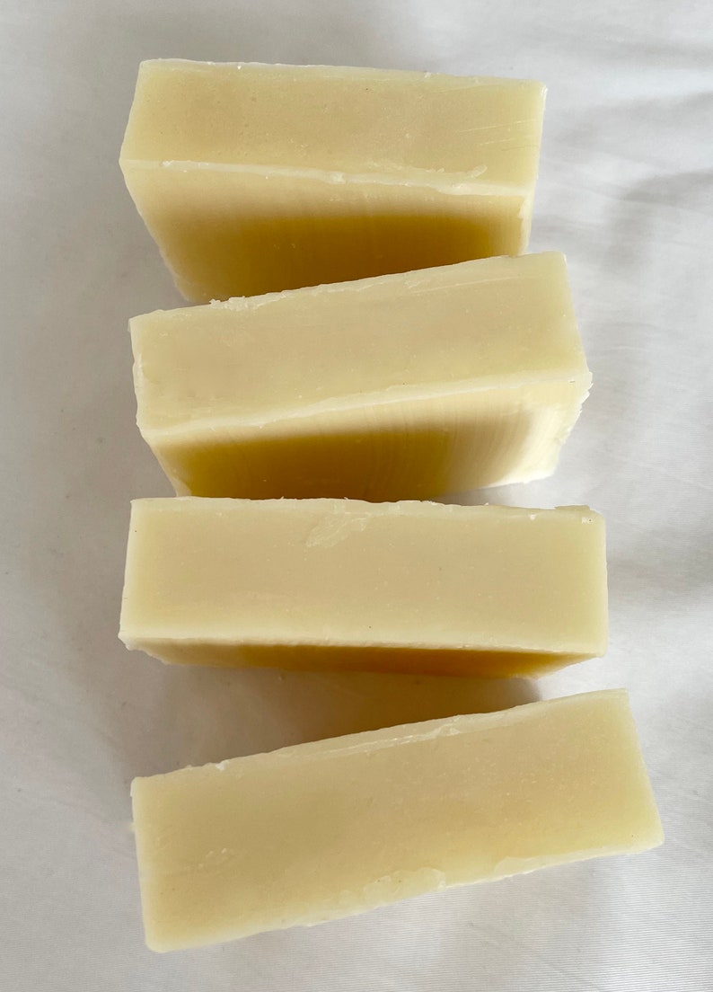 May include: Four bars of plain white soap stacked on top of each other on a white surface.