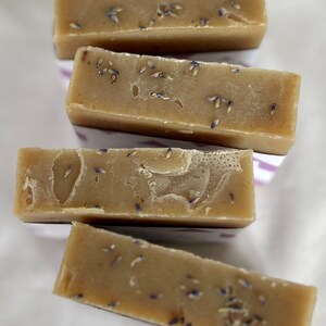 Puede incluir: Cuatro pastillas de jab&oacute;n rectangulares de color tostado apiladas en disposici&oacute;n escalonada. Cada pastilla tiene una textura suave y s&oacute;lida con peque&ntilde;os capullos de lavanda morados secos incrustados por toda la superficie.