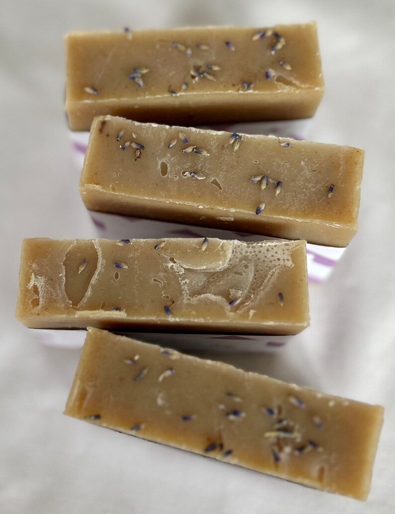 Puede incluir: Cuatro pastillas de jab&oacute;n rectangulares de color tostado apiladas en disposici&oacute;n escalonada. Cada pastilla tiene una textura suave y s&oacute;lida con peque&ntilde;os capullos de lavanda morados secos incrustados por toda la superficie.