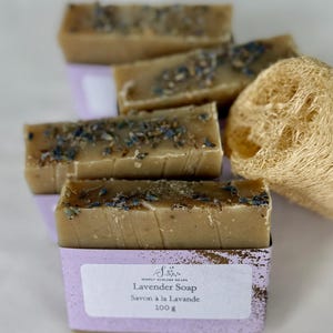 Puede incluir: Cuatro barras de jab&oacute;n rectangulares de color tostado cubiertas con brotes de lavanda secos. Cada barra est&aacute; envuelta en una etiqueta de papel morado claro con el texto Simply Sublime Soaps, Lavender Soap, Savon &agrave; la Lavande y 100 g. Se incluye una esponja de lufa natural.