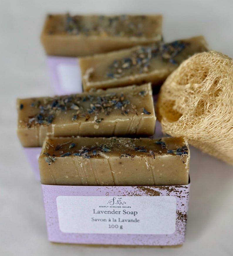 Puede incluir: Cuatro barras de jab&oacute;n rectangulares de color tostado cubiertas con brotes de lavanda secos. Cada barra est&aacute; envuelta en una etiqueta de papel morado claro con el texto Simply Sublime Soaps, Lavender Soap, Savon &agrave; la Lavande y 100 g. Se incluye una esponja de lufa natural.