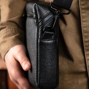 May include: A black leather messenger bag with a zipper closure and an adjustable strap. The bag has a textured surface and a sleek design.