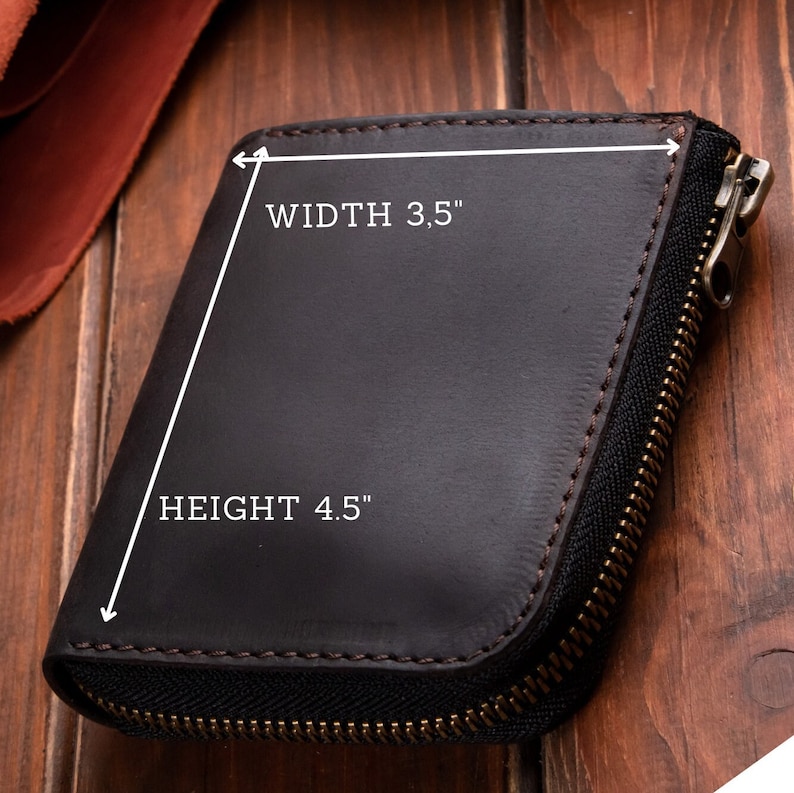 May include: A dark brown leather wallet with a wrap-around zip closure and visible stitching. The wallet features a width of 8.89 cm and a height of 11.43 cm as indicated by the white text and arrows printed directly on the surface of the item.