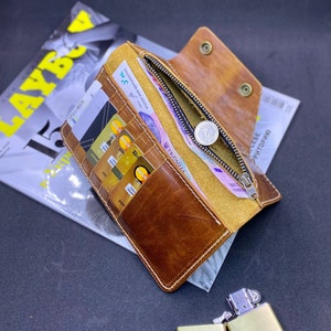 Puede incluir: Una cartera de cuero color canela con m&uacute;ltiples ranuras para tarjetas, un compartimento para monedas con cremallera y tirador plateado, y cierre de bot&oacute;n a presi&oacute;n. El interior contiene varias tarjetas y billetes con texto en ucraniano.
