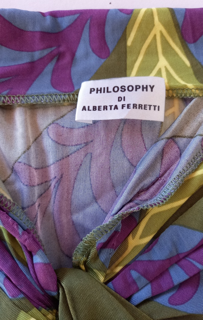 May include: A close-up of a green, purple, and blue patterned fabric with a white tag that reads "PHILOSOPHY DI ALBERTA FERRETTI".