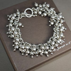 May include: A silver bracelet with a toggle clasp and a design of many small silver balls. The bracelet is displayed on a brown box with the text "Find yourself in it".
