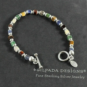 Puede incluir: Un brazalete de piedras preciosas multicolores con un cierre de palanca de plata. El brazalete presenta piedras de forma cuadrada en tonos de azul, verde, marrón y amarillo. El brazalete está hecho por Silpada Designs y se describe como "Joyería fina de plata de ley".