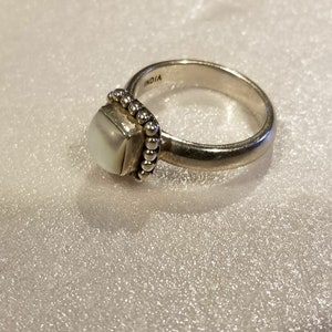 May include: A silver ring with a white square stone and a beaded band. The band is inscribed with the word "INDIA".