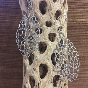 May include: A pair of silver filigree earrings in a teardrop shape. The earrings are made of delicate, intricate wirework and have a modern, minimalist design.