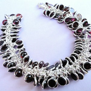 May include: A silver bracelet with a chain design and multiple dark purple gemstones. The bracelet is made of metal and has a clasp closure.