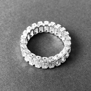May include: A silver ring with a row of clear, rectangular-shaped stones set in a continuous band.