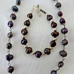 May include: A set of black pearl jewelry featuring a necklace and bracelet. The necklace is made of black pearls strung on a silver chain. The bracelet is made of black pearls and silver beads.