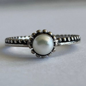 May include: A silver ring with a white pearl set in a beaded bezel. The band is also beaded.