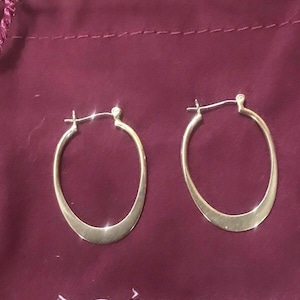 May include: A pair of gold oval hoop earrings on a burgundy velvet pouch with the word "SILPAD" printed on it.