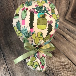 May include: A white scrub hat with a green, pink, and blue cactus print. The hat is tied with a green ribbon.