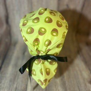 May include: A green scrub hat with a kiwi fruit print. The hat has a black ribbon tie.