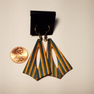 May include: A pair of wooden earrings with a geometric shape. The earrings are striped with yellow, blue, and green colors. The earrings have a cutout design.