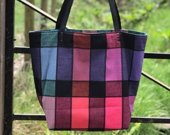 May include: A large tote bag with black leather straps and a colorful plaid pattern in shades of pink, purple, blue, green, and black.