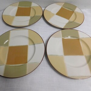 May include: A set of four round ceramic plates featuring a checkered pattern in shades of mustard yellow, sage green, and white. Each plate has a smooth, glossy finish and a thin, dark-colored rim, arranged in a two-by-two grid formation.