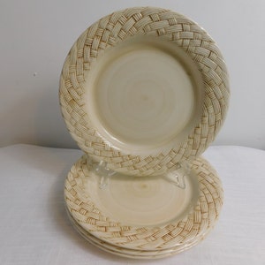 May include: A set of three round ceramic plates featuring a cream-colored center with a subtle swirl pattern and a raised, textured rim designed to resemble a woven basket weave pattern in shades of light tan and beige throughout the surface.