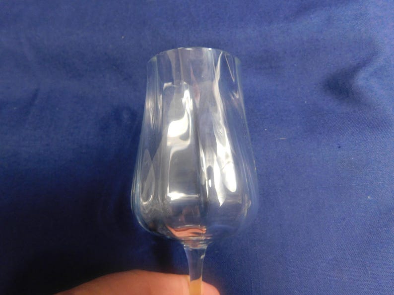 May include: A clear wine glass with a tulip-shaped bowl and vertical ridges. The glass is held against a blue background. The stem is thin and the glass is empty.