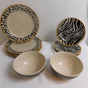May include: A set of beige ceramic dinnerware with animal print designs. The set includes plates with leopard print borders and zebra print accents, along with matching bowls. The plates have a gold trim.