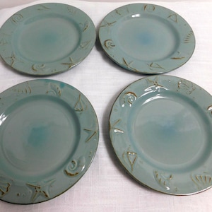 May include: Four aqua-colored ceramic plates with embossed nautical designs. Each plate features a central well and a rim decorated with sailboats, shells, and starfish. The plates are approximately 8 inches in diameter.