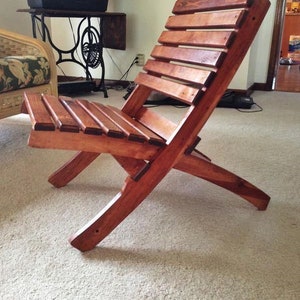 May include: A wooden folding chair with a natural wood finish. The chair has a slatted back and seat, and the legs are curved. The chair is sitting on a light-colored carpet.