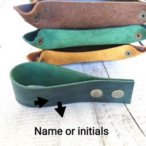 A dark green leather tray with two brass rivets. The tray is labeled 'Name or initials' and has two arrows pointing to the area where the name or initials would be added.