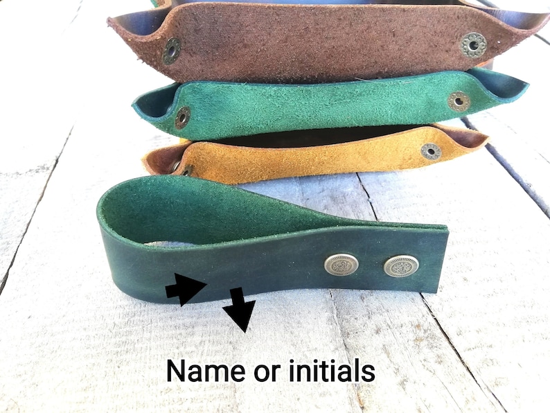 A dark green leather tray with two brass rivets. The tray is labeled 'Name or initials' and has two arrows pointing to the area where the name or initials would be added.