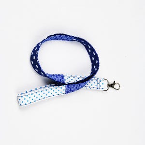 Könnte beinhalten: Ein blaues und weißes gemustertes Lanyard mit einem silbernen Drehverschluss. Das Lanyard ist aus Stoff und hat auf einer Seite ein Punkte-Muster und auf der anderen Seite ein Blumenmuster.