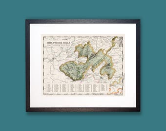 Könnte beinhalten: Eine gerahmte topografische Karte mit dem Titel Shropshire Hills Area of Outstanding Natural Beauty. Die Karte zeigt eine detaillierte Reliefdarstellung des Geländes in Grün- und Beigetönen, überlagert von einem Raster mit einer nummerierten Liste.