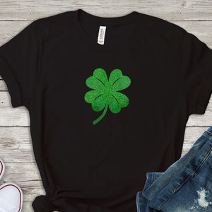 Może przedstawiać: Czarny T-shirt z zielonym brokatowym wzorem koniczyny czteroliściennej.