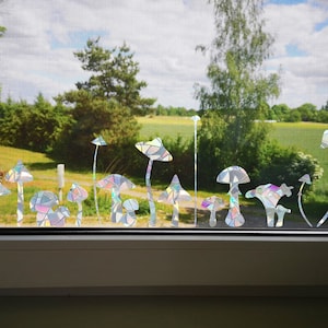 Könnte beinhalten: Ein Fenster mit Blick auf ein grünes Feld und Bäume. Das Fenster ist mit einer Reihe von regenbogenfarbenen Pilzaufklebern verziert.